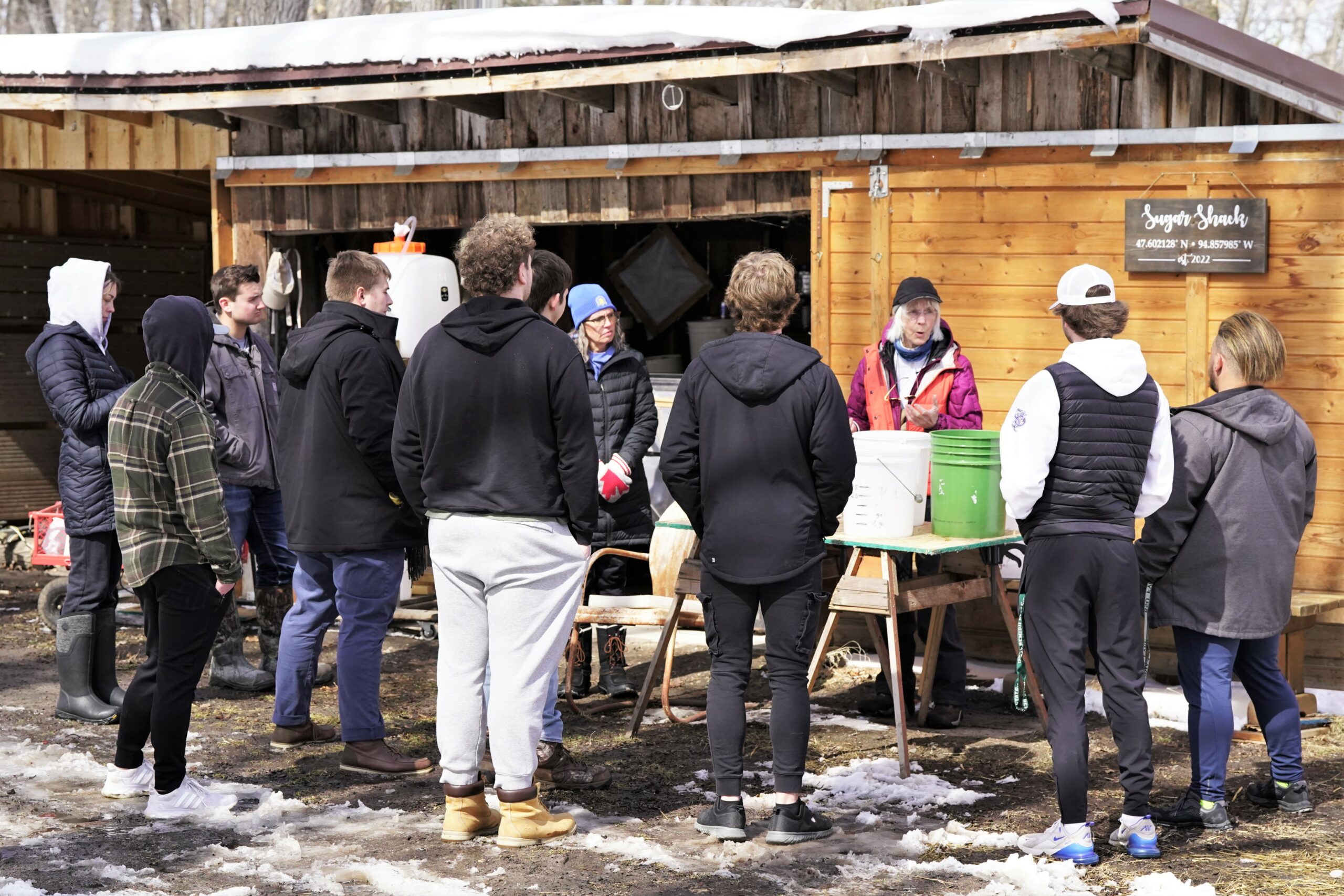 A group of Bemidji State students from Sherry Holloway's People of the Environment class listen to Mur Gilman, third from right, explain the process of her maple syrup operation on Thursday, April 6, 2023, north of Bemidji. (Micah Friez / Bemidji State)