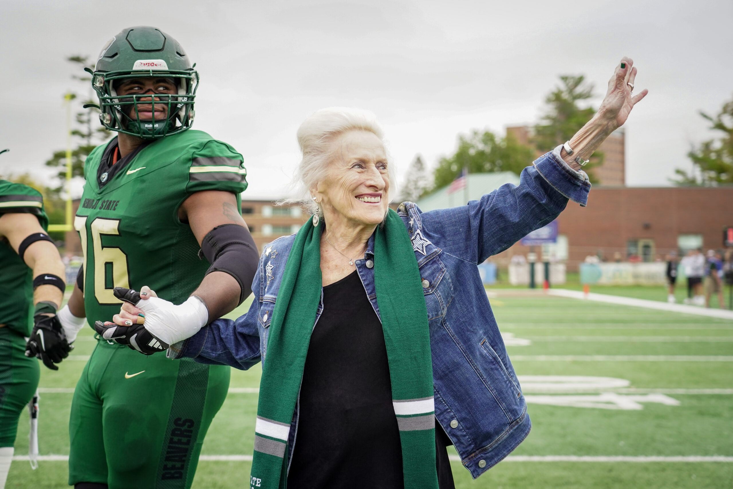 Margaret Laurich waves to the crowd while walking to midfield for the pregame coin toss with Ty Cobb (76) and the Bemidji State football captains before the Homecoming football game against Minnesota State on Saturday, Sept. 30, 2023, at Chet Anderson Stadium. Laurich, a 1963 Bemidji State College graduate, returned to Bemidji for the first time in 60 years for Homecoming weekend. (Micah Friez / Bemidji State)